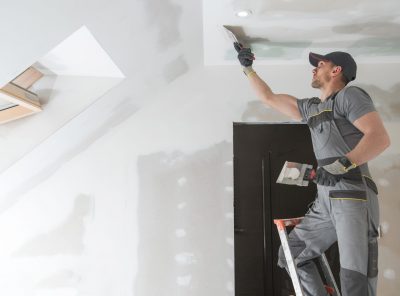 Finishing and Patching Drywall Walls by Caucasian Remodeler in His 30s. Construction Industry.