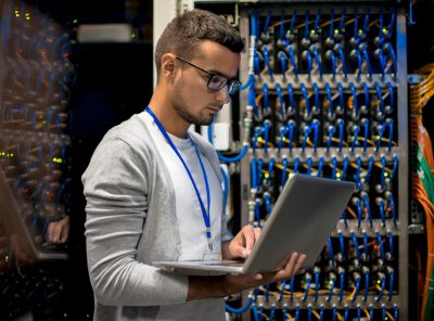 Side view  portrait of young man with laptop standing by server cabinet while working with supercomputer